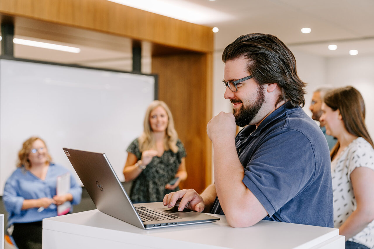 Image of man with laptop surrounded by colleagues